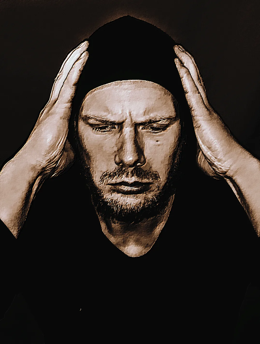 Distraught man with hood on and facial hair gripping his head with his hands