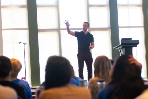 Russell-standing-on-stage-with-his-hand-in-the-air